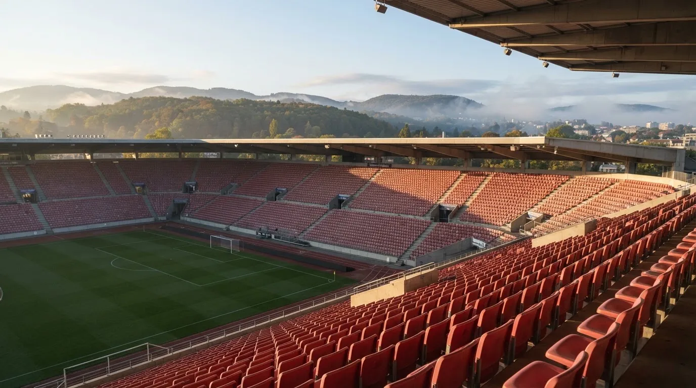 Ein leeres Stadion im Morgenlicht mit Blick auf die Sitzreihen, im Hintergrund Hügel und aufsteigender Nebel.