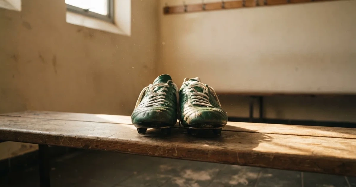 Ein Paar Fussballschuhe steht auf einer Holzbank in einer leeren Umkleide, Morgenlicht fällt durch ein kleines Fenster.
