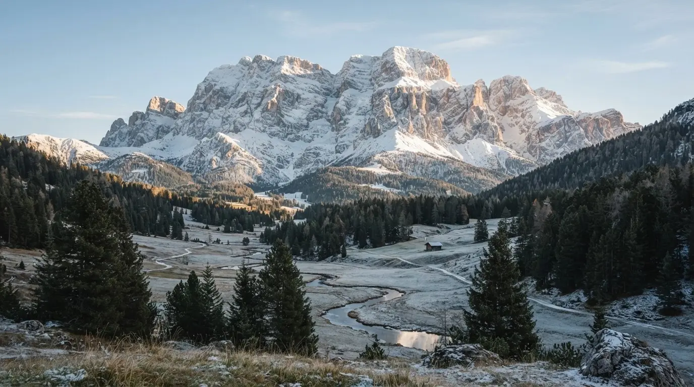 Eine verschneite Bergkette erhebt sich über einem stillen Tal, der Himmel darüber ist klar und von blassem Blau.