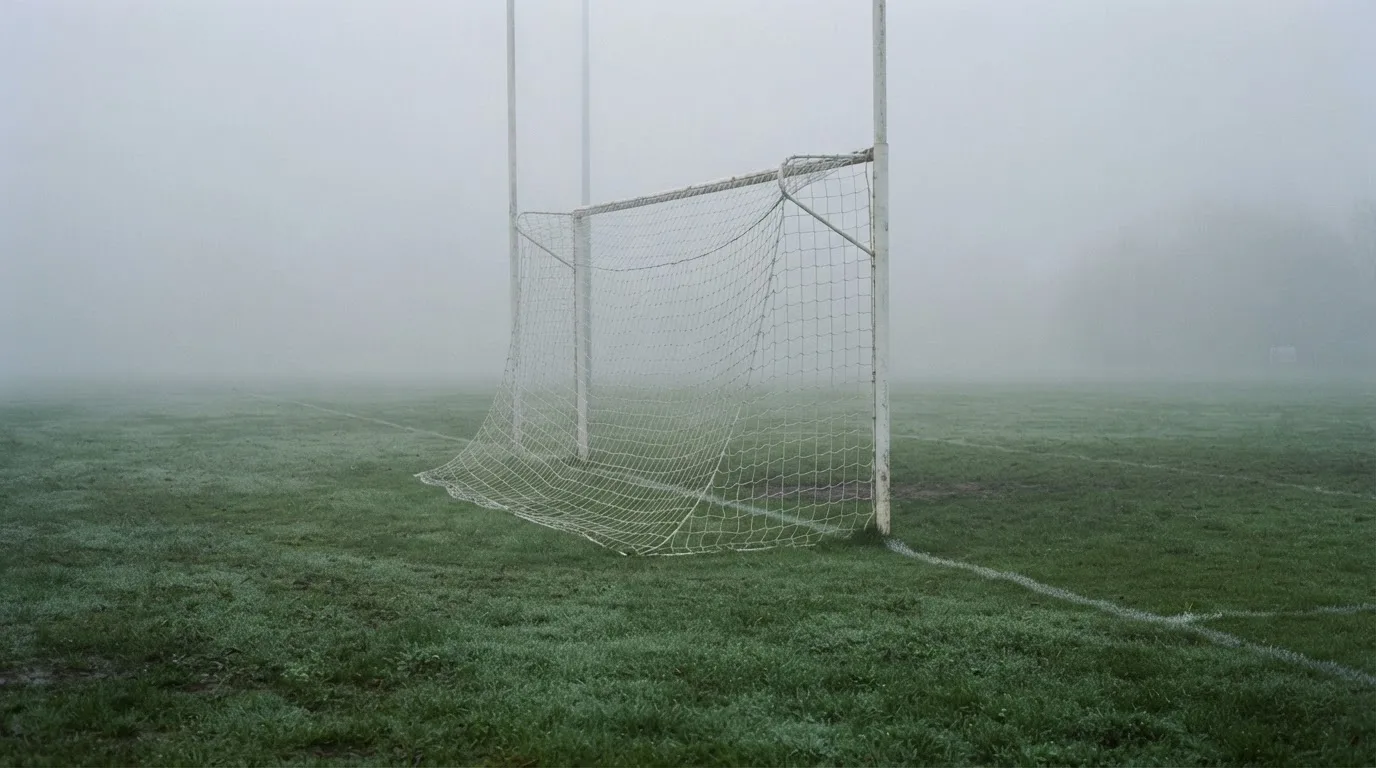 Eine Torlinie mit Netz steht am frühen Morgen im dichten Nebel auf einem Rasenplatz, die Umrisse der Pfosten verschwimmen.