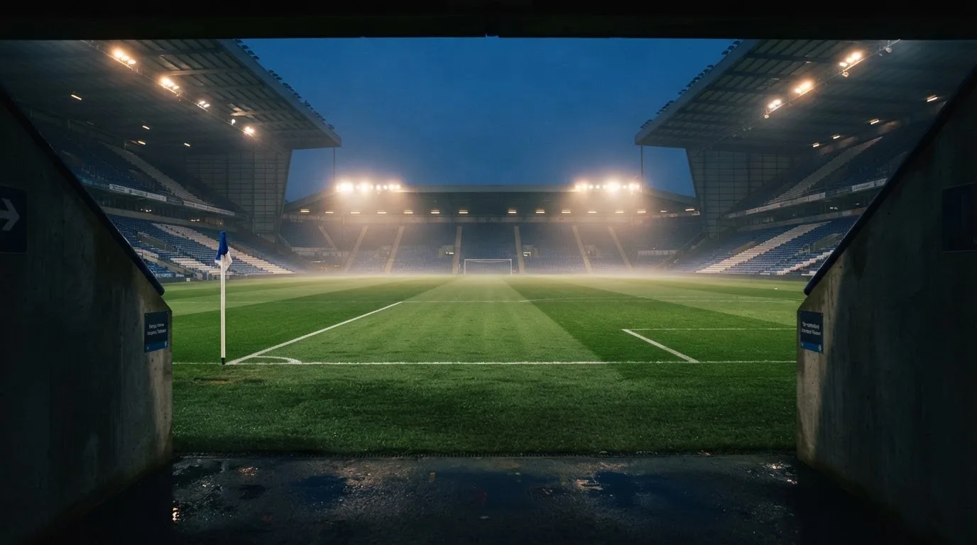 Leere Tribünenränge eines Fussballstadions in der Abenddämmerung, über dem Rasen leuchten die Flutlichter.
