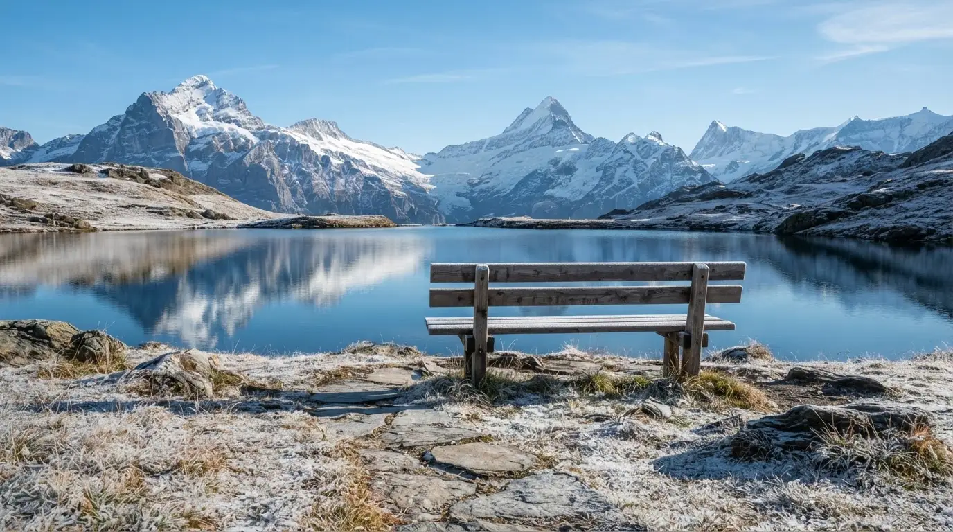 Eine Bank an einem Bergsee, dahinter schneebedeckte Gipfel im klaren Licht eines Wintermorgens.