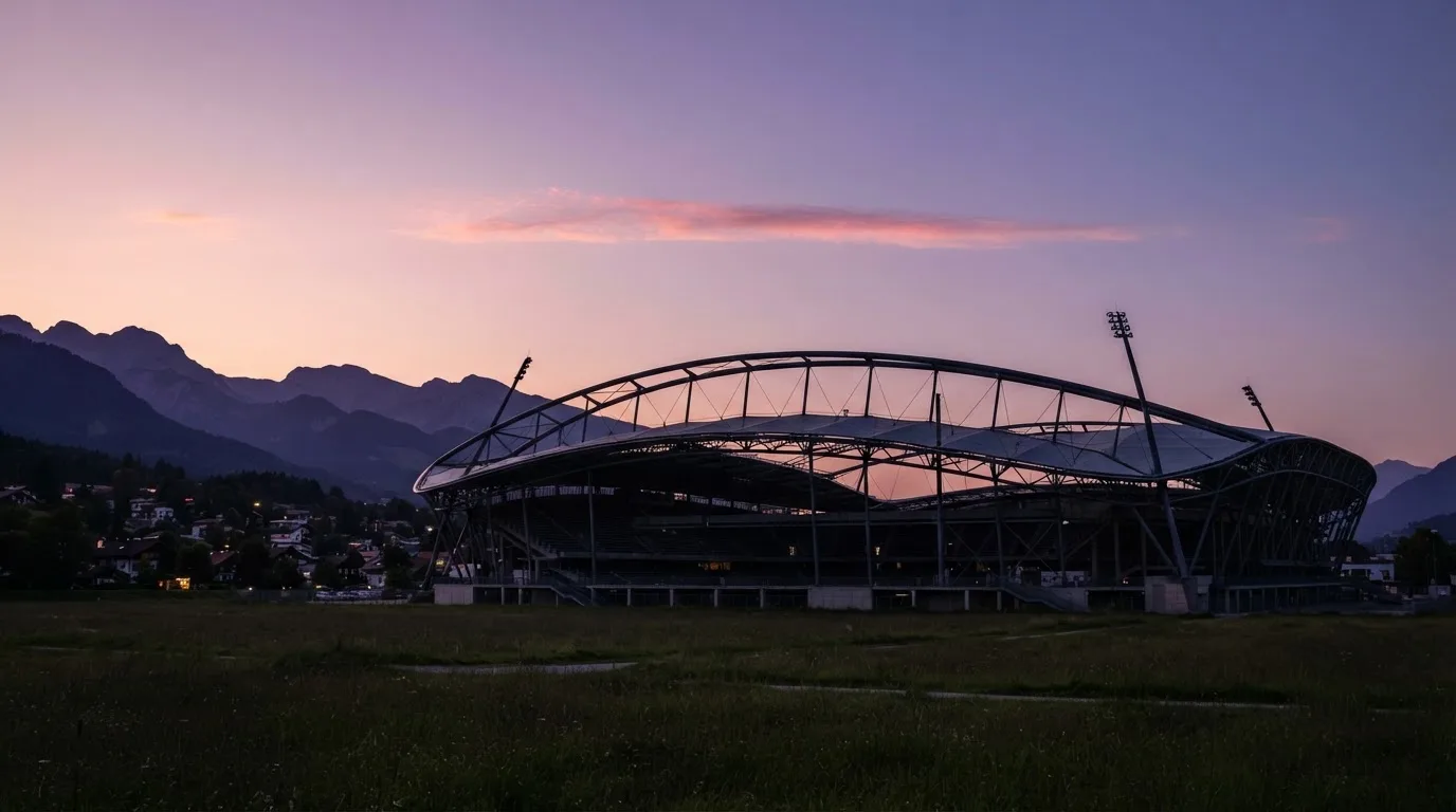 Die Silhouette eines Stadiondachs vor dem violetten Abendhimmel, dahinter eine Hügelkette.