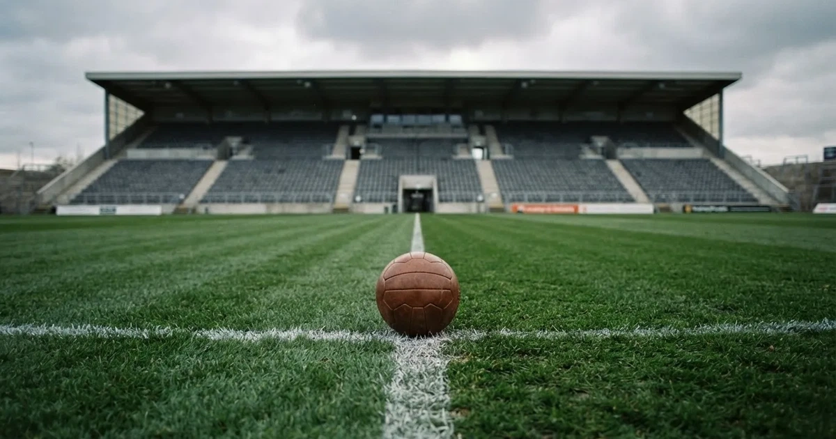 Ein Fussball liegt auf dem Anstosspunkt eines frisch gemähten Rasens, dahinter eine grosse Tribüne unter bewölktem Himmel