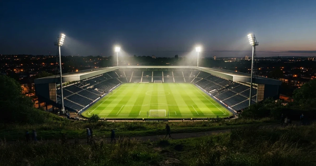 Ein Fussballstadion bei Flutlicht von einer Anhöhe aus gesehen, der Rasen leuchtet grün unter dunklem Abendhimmel