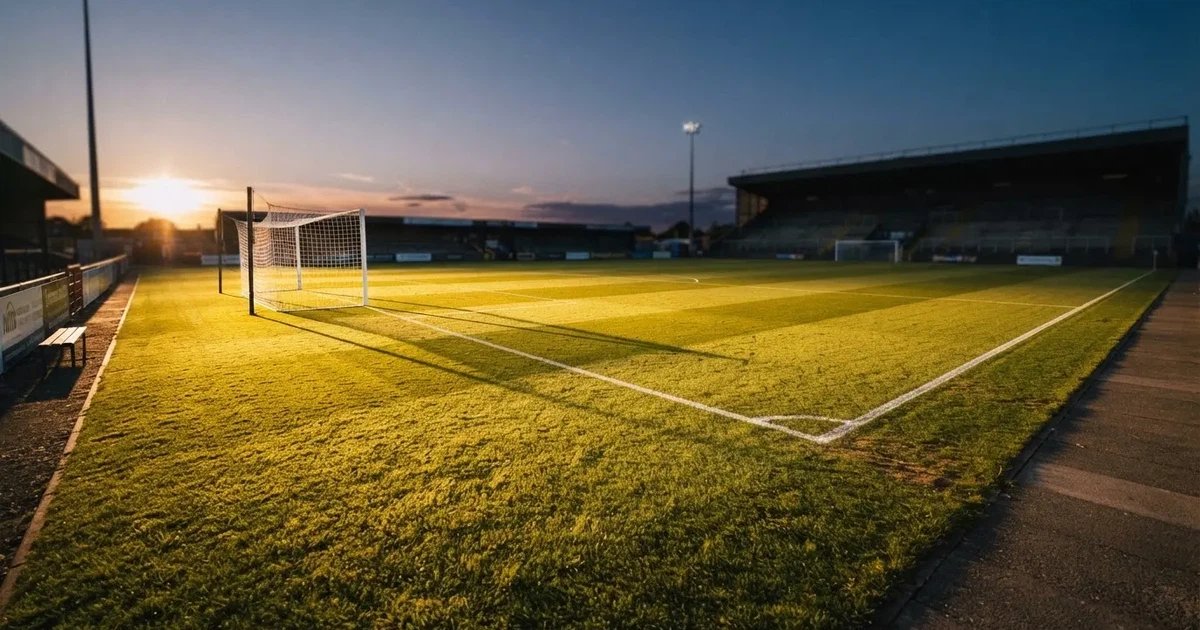 Ein Fussballplatz im Abendlicht mit langen Schatten der Torpfosten, die Rasenfläche leuchtet gelblich.