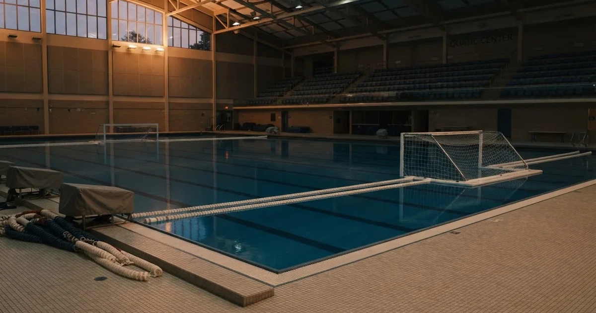Ein Wasserballbecken am Abend mit zwei schwimmenden Torrahmen an den Enden, ruhiges blaues Wasser, leere Ränge.