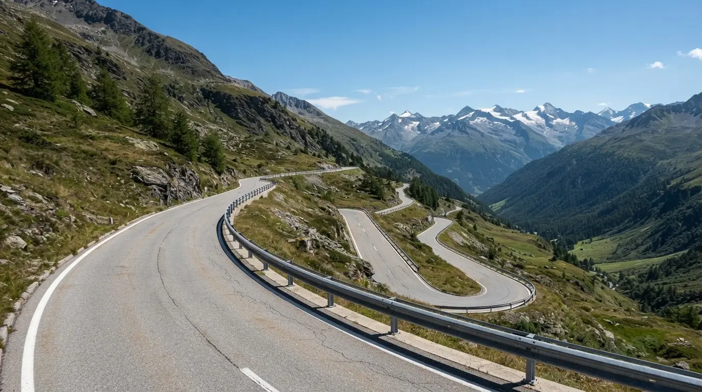 Eine Passstrasse mit Leitplanke windet sich an einem klaren Tag durch eine Berglandschaft.