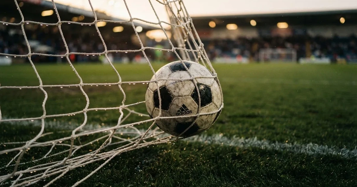 Ein Fussballnetz in Nahaufnahme, in dem ein Ball hängt, Wassertropfen glänzen auf den Maschen.