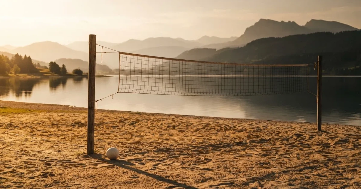 Ein Volleyballnetz am Sandstrand eines Sees, späte Nachmittagssonne, das Wasser liegt glatt im Hintergrund