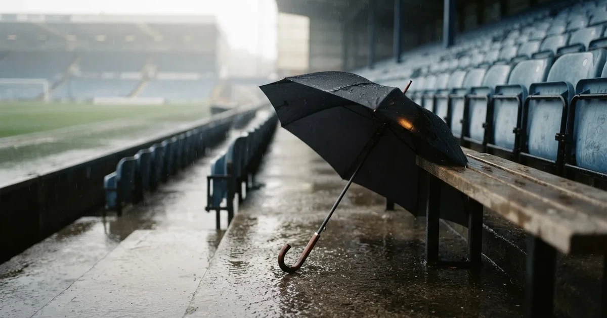 Ein offener Regenschirm lehnt an einer leeren Tribünenbank, Regen fällt auf die Stufen eines Stadions