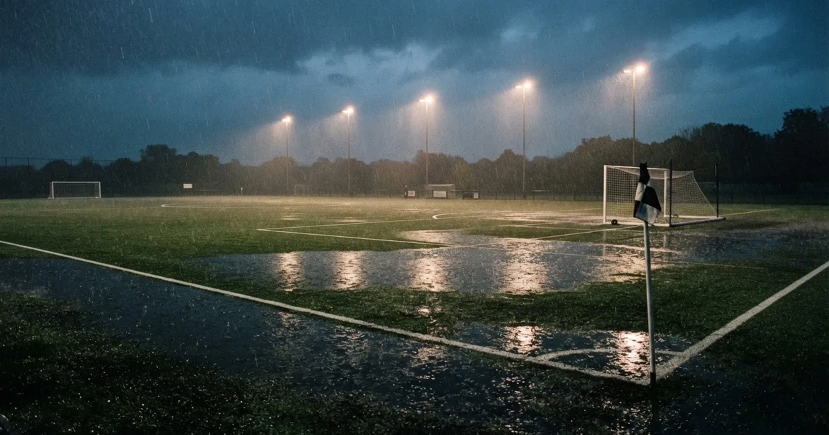 Ein Fussballplatz mit Kunstrasen im Regen, Pfützen spiegeln das Licht der Flutlichtmasten