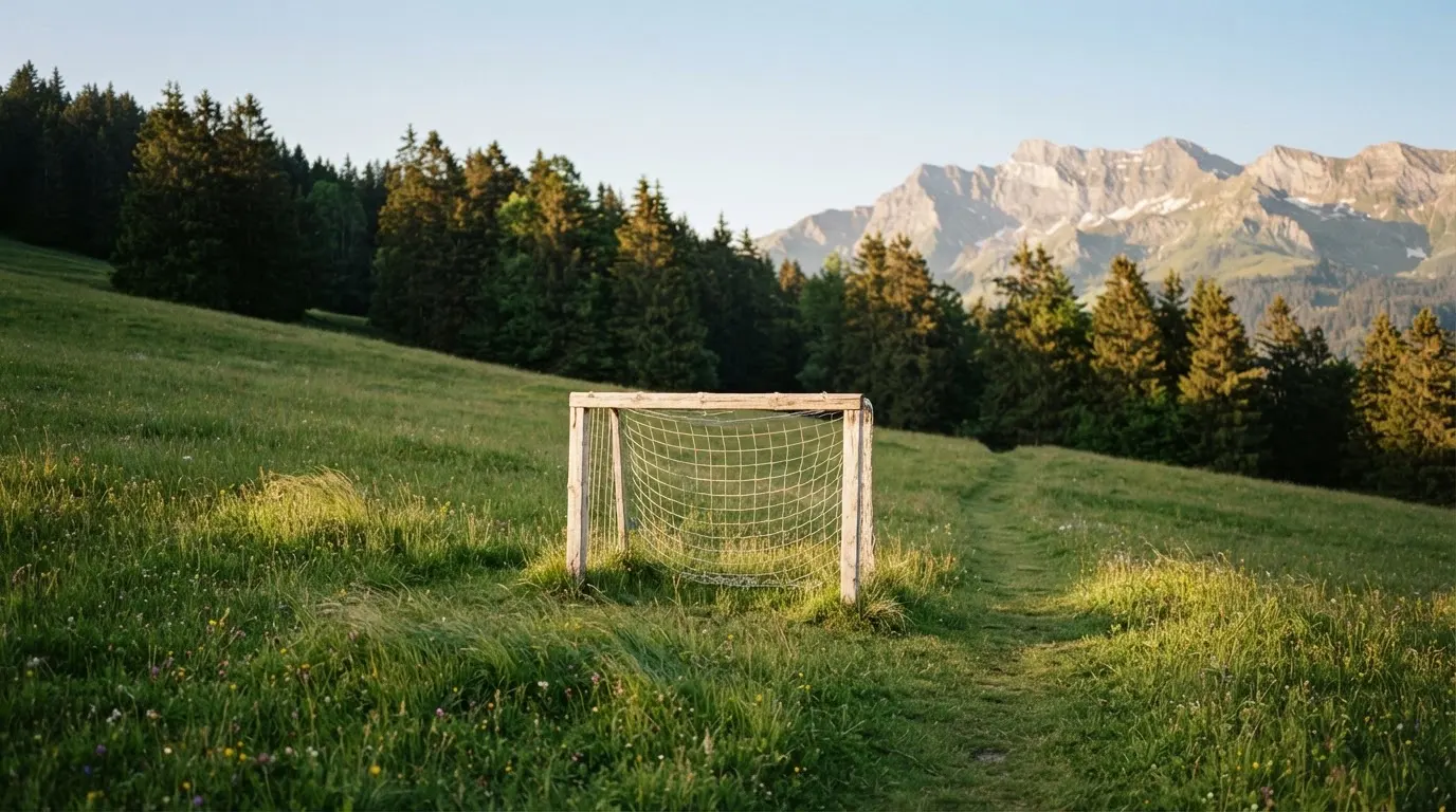 Eine Almwiese mit einem kleinen Holztor für Kinderfussball, dahinter erheben sich bewaldete Hänge im Nachmittagslicht.