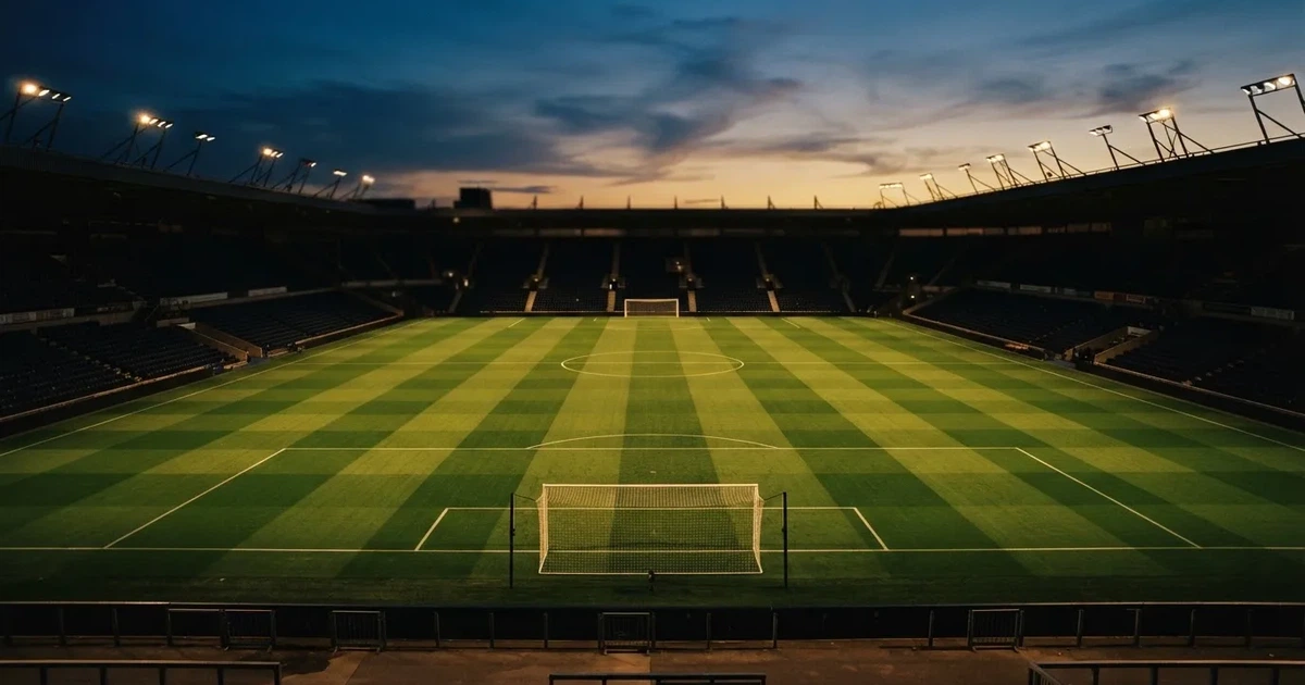 Ein menschenleerer Fussballplatz mit frisch gemähtem Rasen unter Flutlichtmasten in der Abenddämmerung, aus erhöhter Perspektive fotografiert.