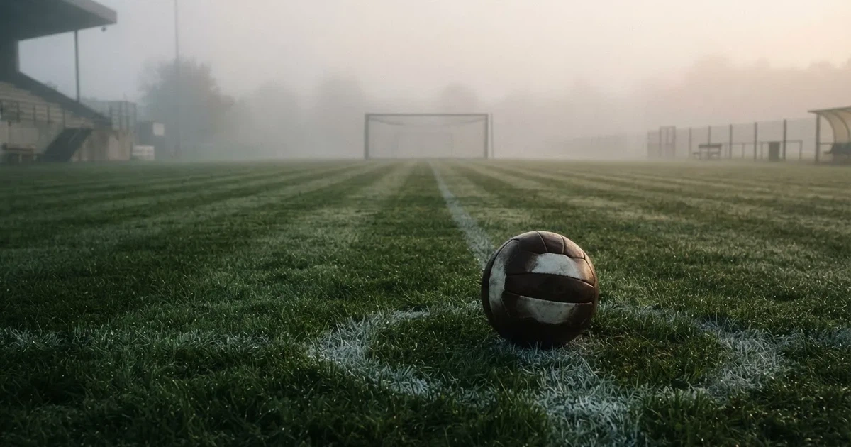 Ein Fussball liegt auf dem Anstosspunkt eines leeren Rasenplatzes im dichten Morgennebel.