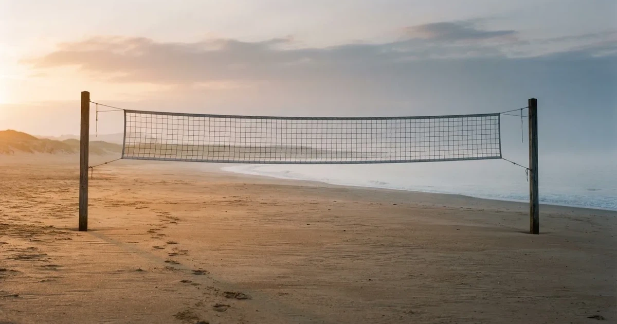 Ein Volleyballnetz spannt sich an einem leeren Sandstrand, das Meer liegt im Dunst.
